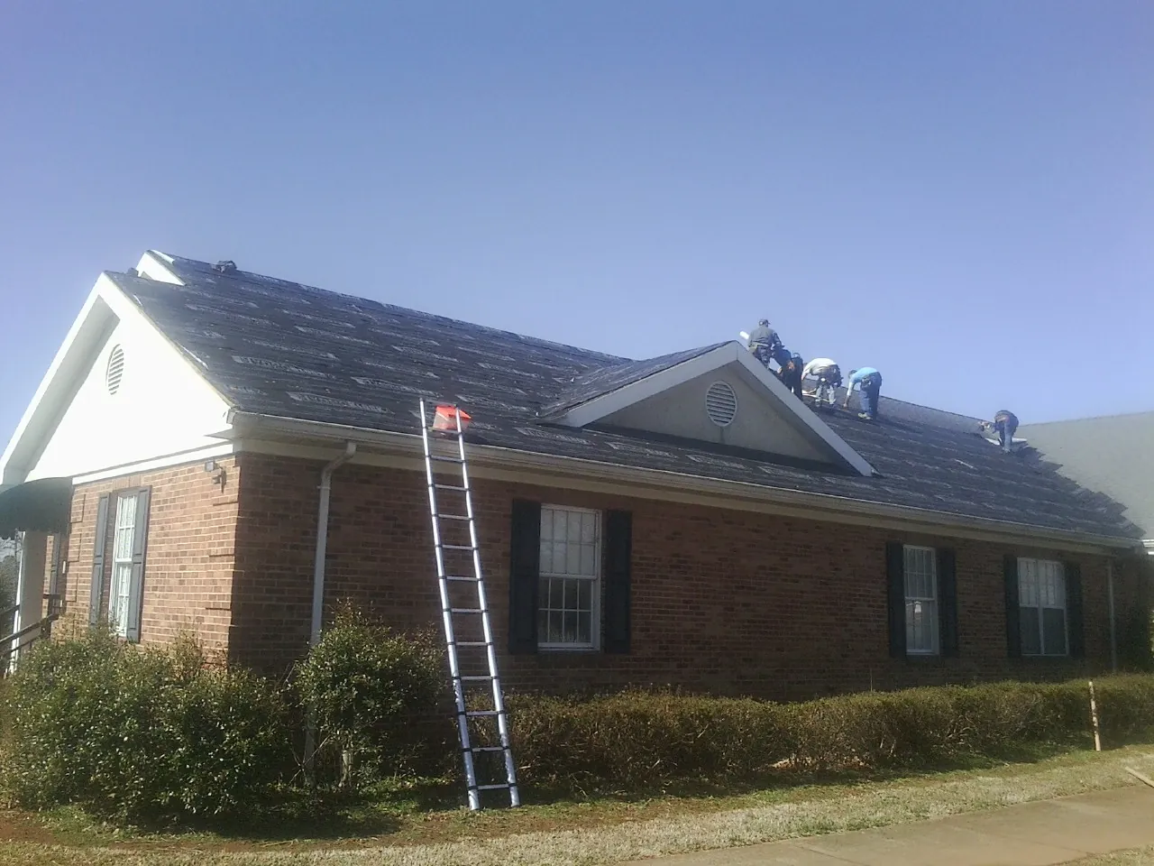 Crew tearing shingles off a brick ranch roof with a ladder set — Metal Roof Repair work by our crew in Yamhill