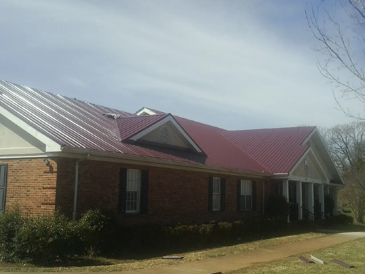Red metal roof with gabled entries on a long brick building, from a Hail Damage Roof Repair job in Yamhill