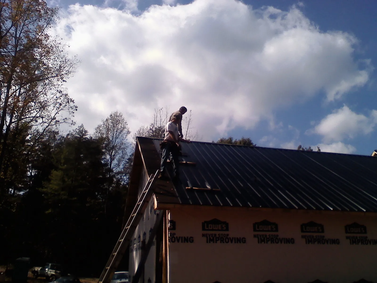 Roofer fastening dark metal panels high against a cloudy sky, from a Roof Inspection job in Yamhill