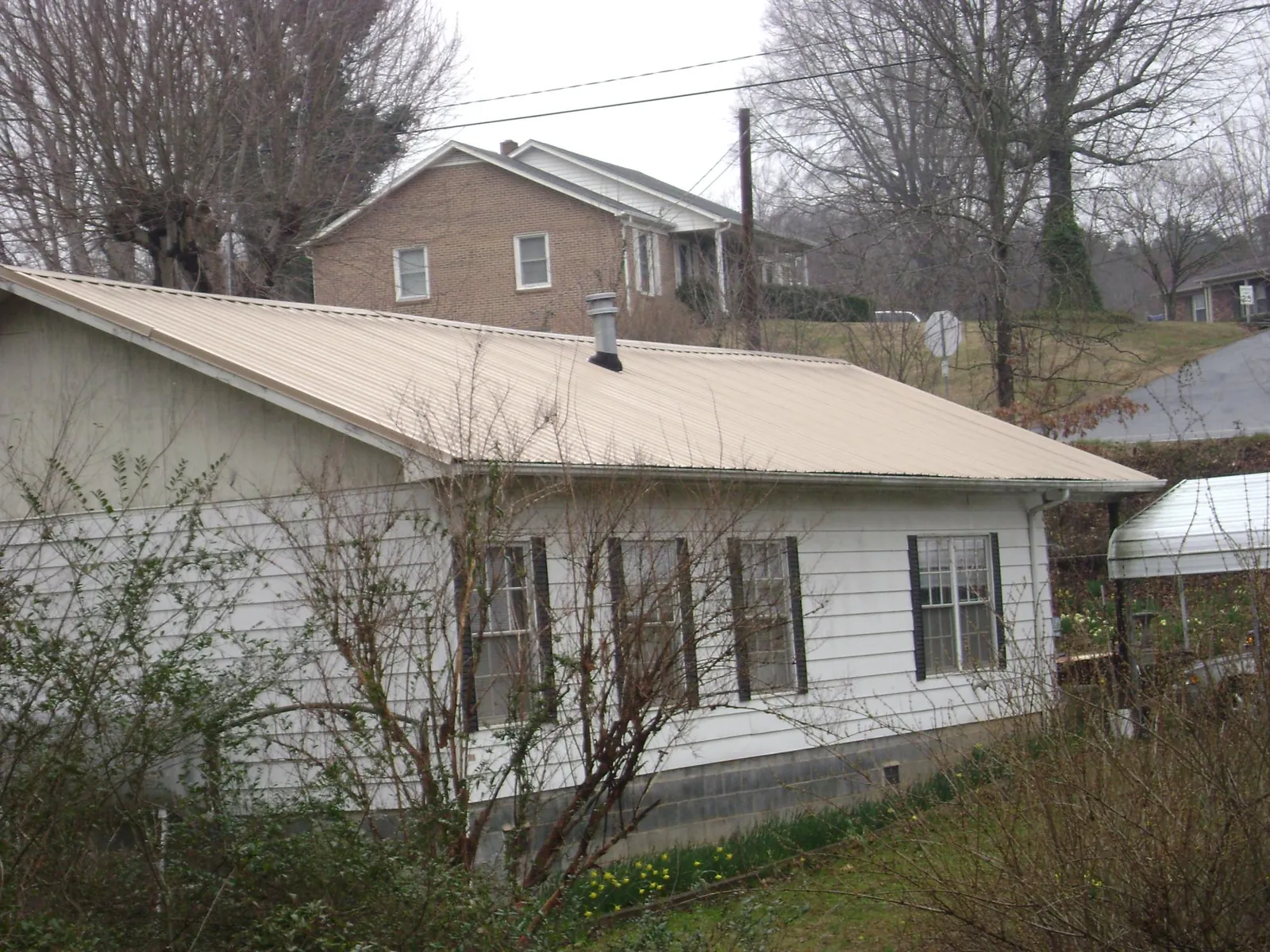 Tan metal roof on a white sided house set into a hillside — Commercial Roofing by Roofing Brothers in Yamhill
